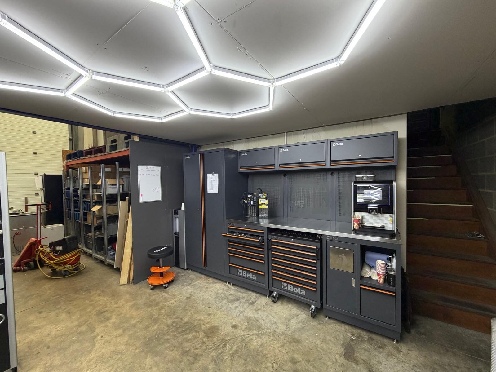 LC Vending Solutions workshop in Basildon — vending machines, parts trolley and hexagonal lighting rig overhead.